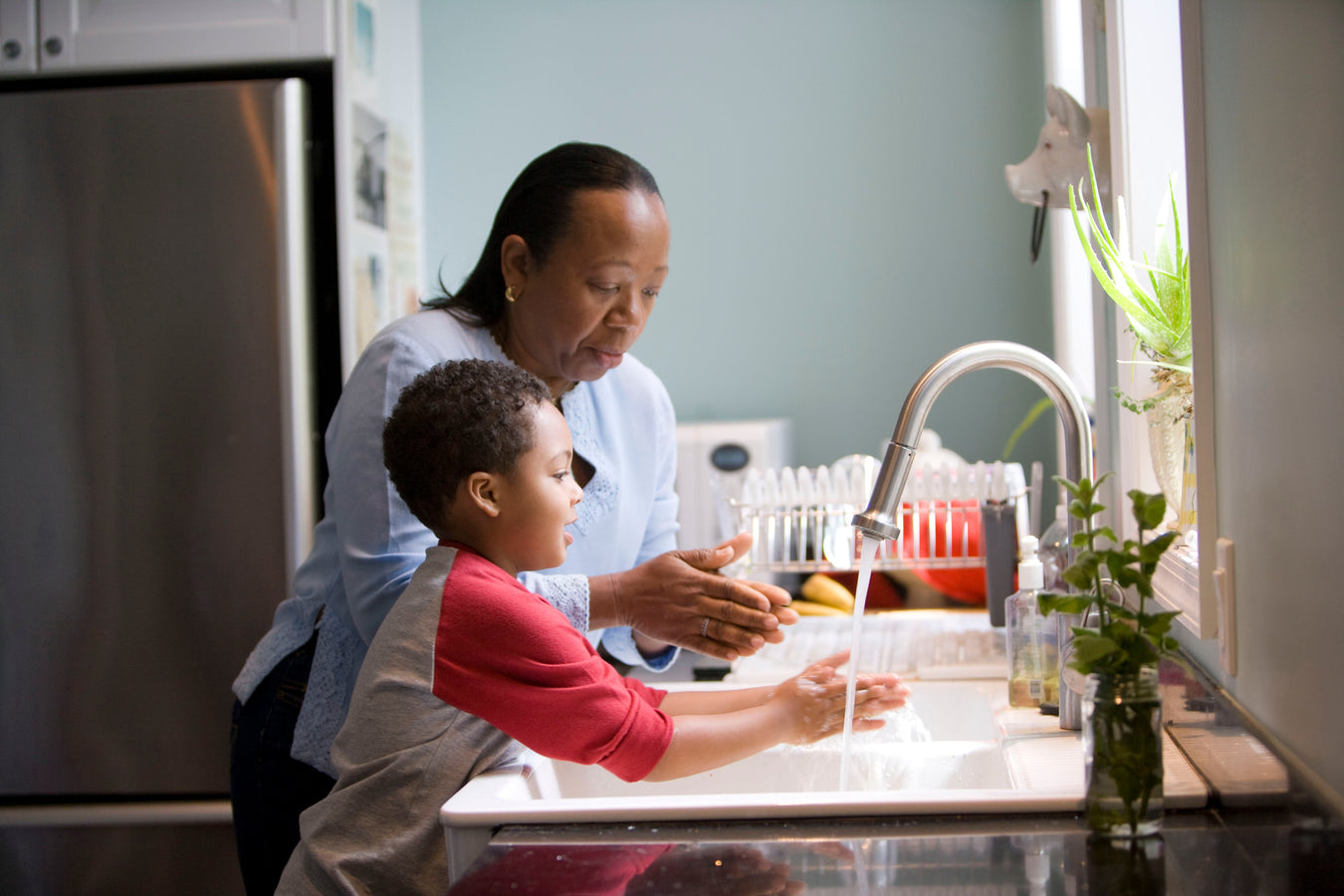 A woman and a child washing dishes side by side, illustrating a shared household responsibility and bonding experience.