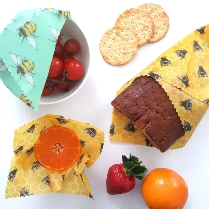 Beeswax wraps being used to wrap food items on a white surface