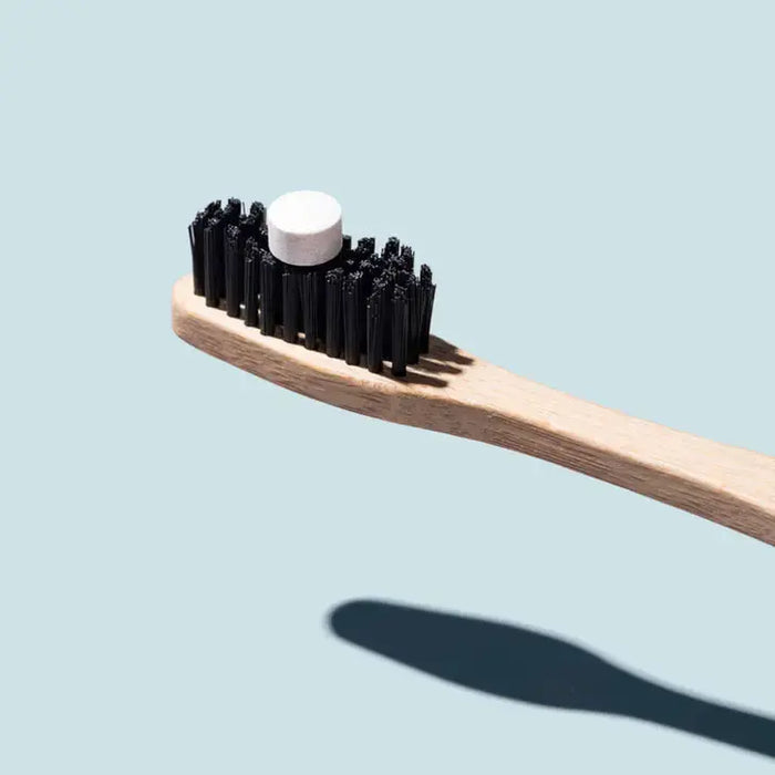 Bamboo toothbrush with black bristles and a white cap on a light blue background