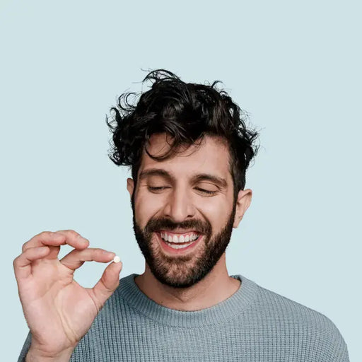 Man with a beard and curly hair holding a small object against a light blue background