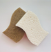 Two natural sponges, one brown and one white, on a light pink background.