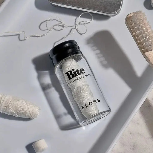Bottle of 'Bite' toothpaste bits floss on a light surface with dental tools.