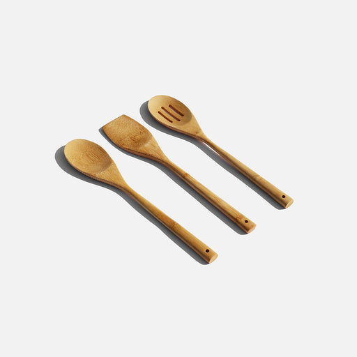 A set of three wooden spoons alongside a wooden spatula, arranged neatly on a light-colored surface.