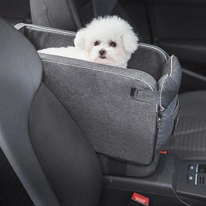 Small white dog sitting in a gray pet car seat inside a vehicle.
