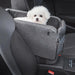 Small white dog sitting in a gray pet car seat inside a vehicle.