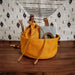 Yellow drawstring bag with brown leather straps on a wooden surface with a patterned curtain in the background.