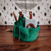 Green bag with brown straps on a wooden surface with a patterned fabric background