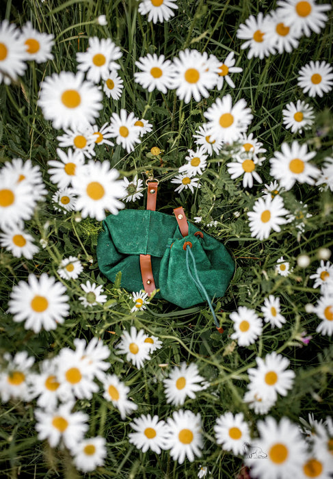 Green bag with brown straps on a bed of white daisies