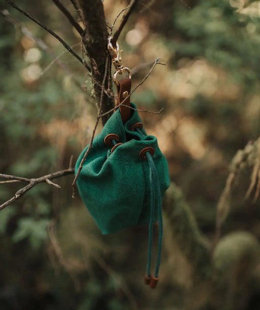 Green drawstring bag hanging on a branch with a blurred natural background