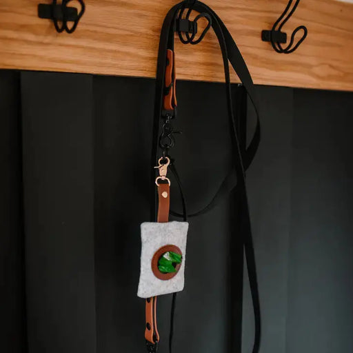 Small pouch with a green stone on a black strap, hanging against a dark background.