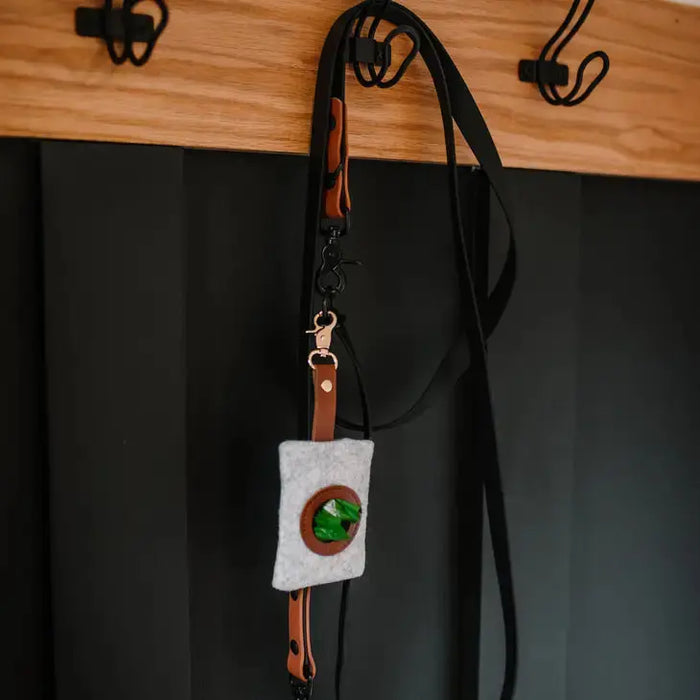 Small pouch with a green stone on a black strap, hanging against a dark background.