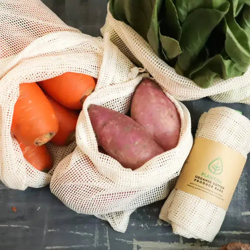 Mesh produce bags with carrots, sweet potatoes, and a roll of organic cotton produce bags on a dark surface.