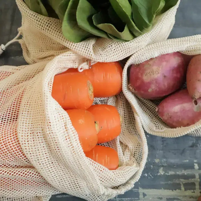 Mesh bags with carrots and potatoes on a textured surface